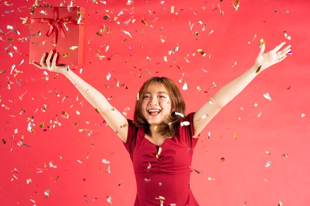 Aziatisch jong meisje in jurk met rode geschenkdoos met vrolijke uitdrukking op roze