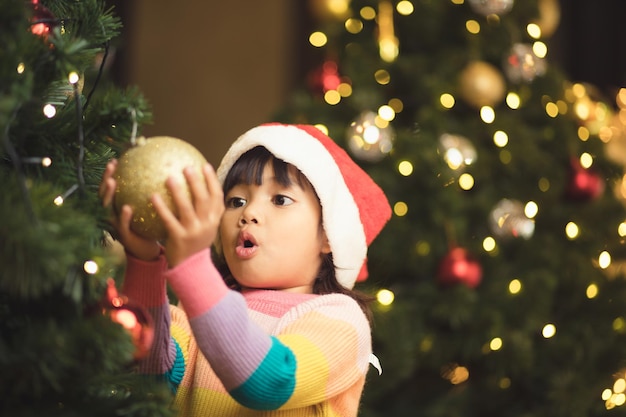 Aziatisch kind dat decoratieve speelgoedbal op kerstboomtak hangt