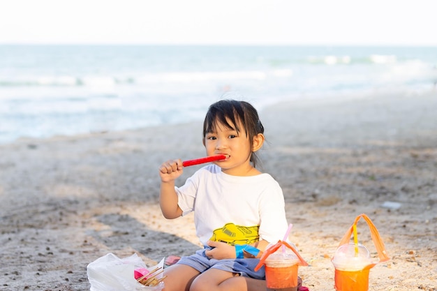 Foto aziatisch kind gelukkig meisje dat voedsel eet op het strand aan zee zomerseizoen