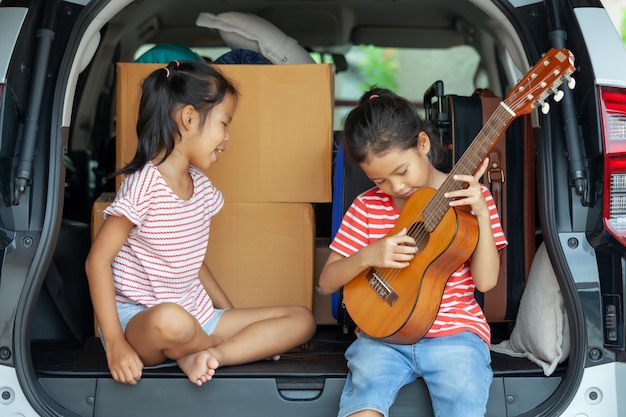 Aziatisch kind meisje gitaar spelen en zingen een lied met haar zus in een auto kofferbak