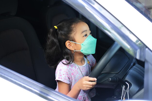 Aziatisch kind met medisch gezichtsmasker dat op de bestuurdersstoel van de auto speelt