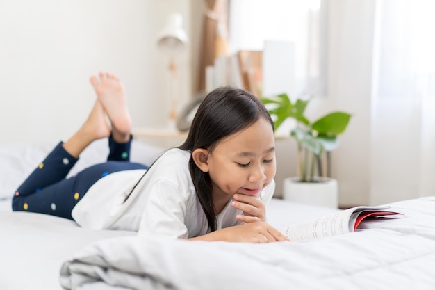 Aziatisch kindmeisje dat boeken leest die thuis op het bed liggen