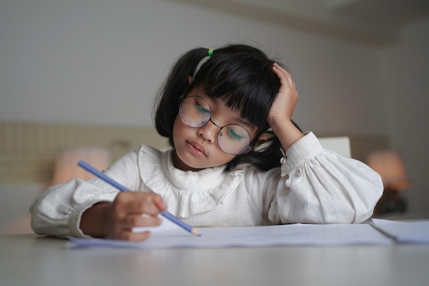 Aziatisch klein kindmeisje dat oogglazen draagt, doet thuis het werk.
