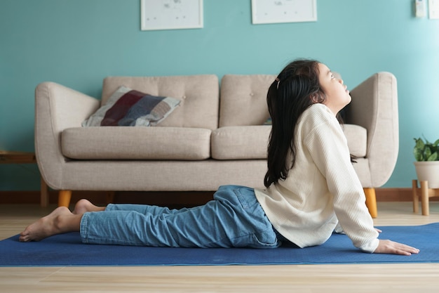 Aziatisch klein meisje dat yoga cobra beoefent, poseert op yogamat in de woonkamer thuis, concept van ontspanning en meditatie