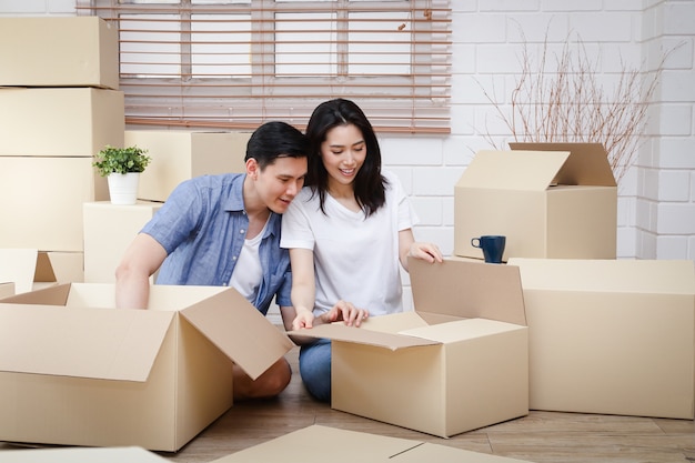 Aziatisch koppel verhuizen naar een nieuw huis Help de bruine papieren doos uitpakken om het huis te versieren. Concept van het starten van een nieuw leven, het opbouwen van een gezin. Kopieer ruimte