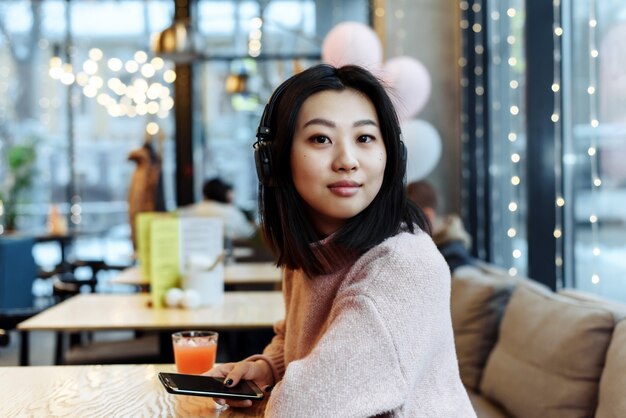 Aziatisch meisje alleen in de stad zit in een café en luistert naar muziek. genieten van muziek op een openbare plek