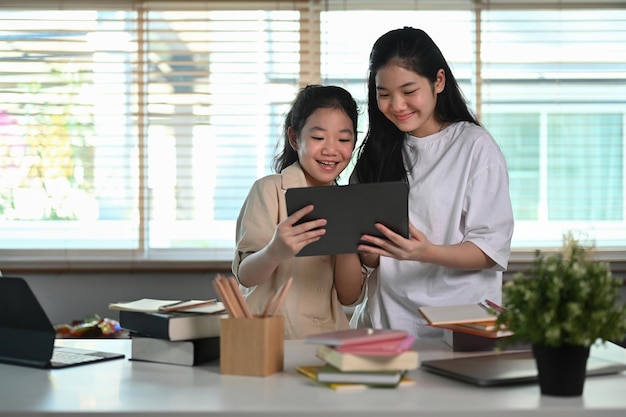 Aziatisch meisje dat digitale tablet gebruikt met haar jongere zus in de woonkamer