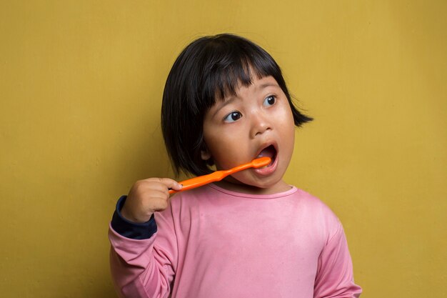 Aziatisch meisje haar tanden poetsen op gele muur