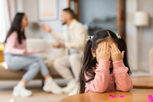 Aziatisch meisje huilende ogen bedekkend terwijl ouders binnen ruzie hebben