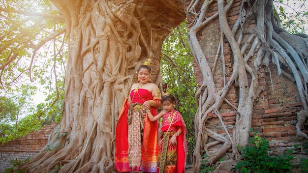 Aziatisch meisje in een Thaise traditionele klederdracht loopt met haar moeder van een oude bakstenen poort met een grote muur van de wortelboom cover