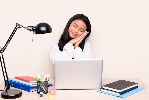 Aziatisch meisje in een werkplaats met laptop op beige muur die slaapgebaar in dorable uitdrukking maken