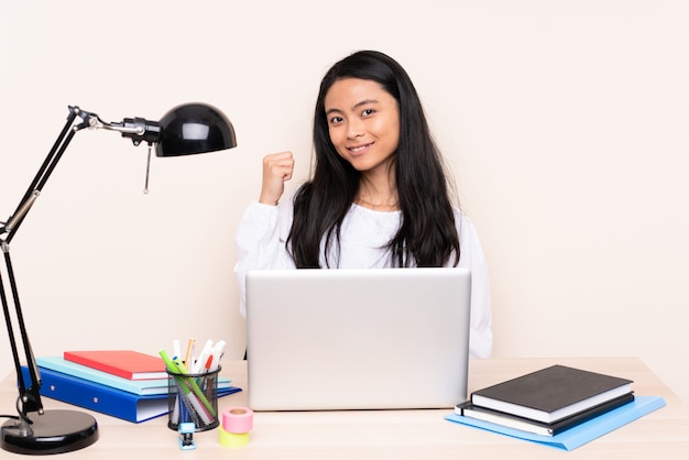 Aziatisch meisje in een werkplek met een laptop op beige muur wijst naar de kant