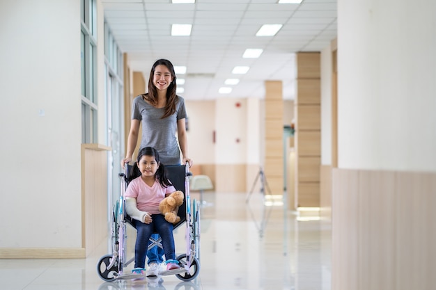 Aziatisch meisje met een gebroken arm die een gipsverband draagt op een rolstoel met haar moeder in het ziekenhuis