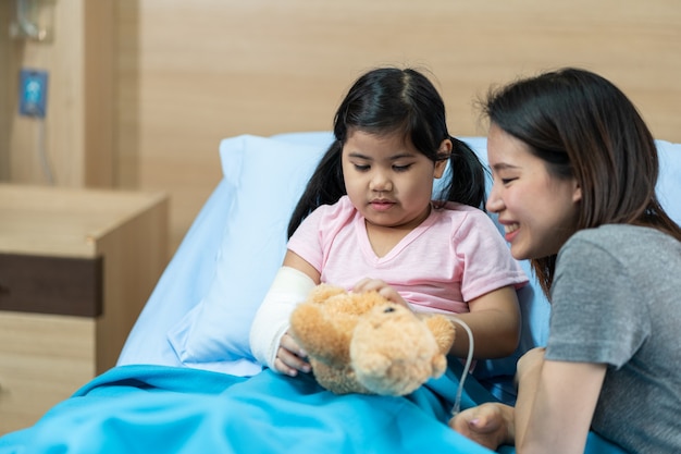 Aziatisch meisje met een gebroken arm in het gips op het ziekenhuisbed met haar moeder