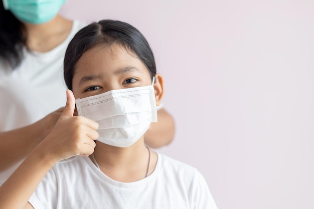 Aziatisch meisje met een medisch beschermend masker en duimen omhoog.