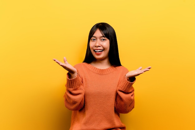 Aziatisch meisje Pretty draagt een oranje casual jurk gele achtergrond Vier de overwinning met een blije glimlach en de uitdrukking van de winnaar met een opgeheven hand blije uitdrukking