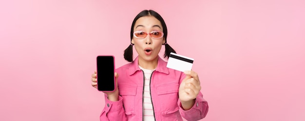 Aziatisch meisje toont scherm van mobiele telefoon en creditcard reageert verrast door camera die onder de indruk st