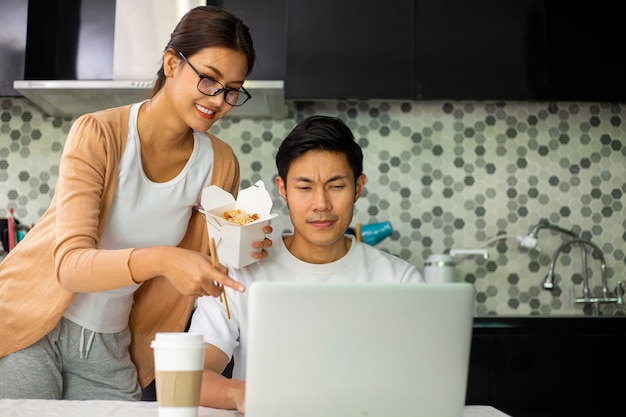 Aziatisch paar dat eet en samenwerkt in de keuken. Geniet van een gezonde maaltijd. Lifestyle voor het avondeten en blijf thuis. vrouw die instant noedels eet.