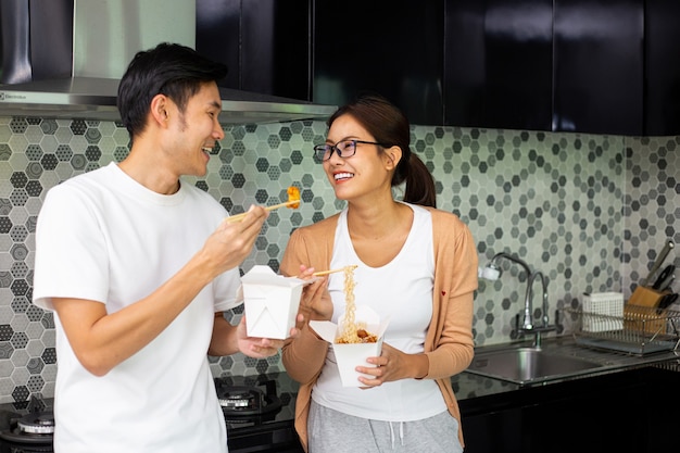 Aziatisch paar die instantnoedels samen eten in de keuken. geniet van een gezonde maaltijd. levensstijl voor het avondeten en blijf thuis. vrouw die instant noedels eet.