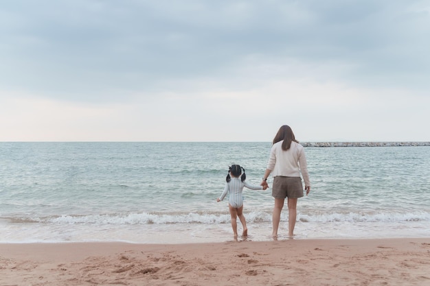 Aziatisch schattig meisje en haar moeder lopen of rennen of spelen op het strand tijdens de zomervakantie Kinderen met prachtig zeezand en blauwe lucht Gelukkige kinderen op vakantie aan zee rennen op het strand