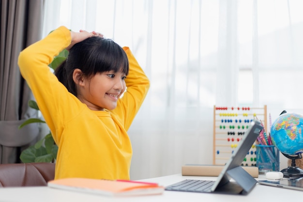Aziatisch schoolmeisje doet haar huiswerk met digitale tablet thuis Kinderen gebruiken gadgets om te studeren Onderwijs en afstandsonderwijs voor kinderen Thuisonderwijs tijdens quarantaine Blijf thuis