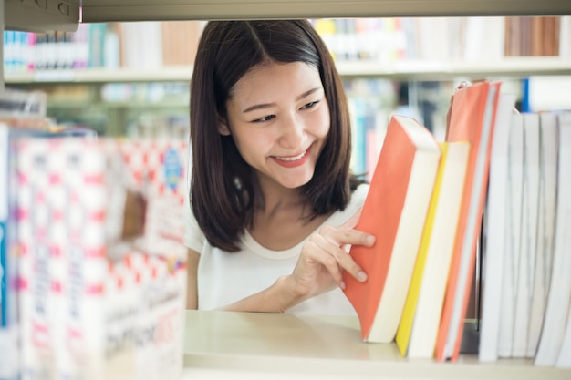 Aziatisch student het zoeken boek voor onderzoek in bibliotheek.