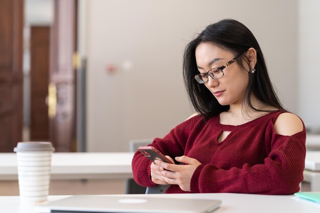 Aziatisch studentenmeisje dat in sociale media op smartphone chat tijdens het studeren in de universiteitsbibliotheek