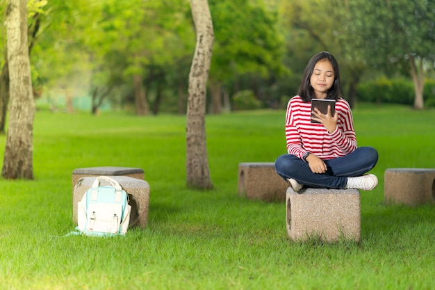 Aziatisch studentenmeisje die een digitale tablet in het schoolpark gebruiken in een zonnige de zomerdag