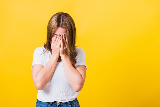 Aziatisch Thais portret mooie jonge vrouw in depressief slecht humeur haar huilende gezicht dicht bij handen, ze sloot haar gezicht omdat ze zich schaamde studio-opname geïsoleerd op gele achtergrond met kopieerruimte