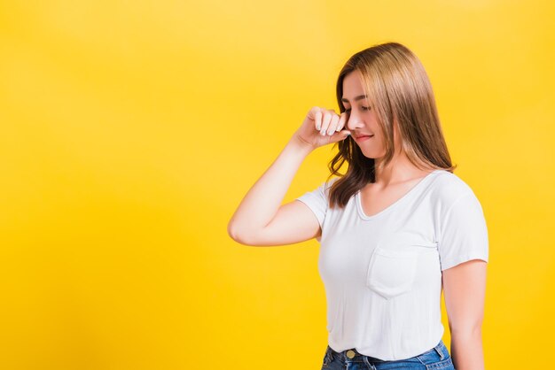 Aziatisch Thais portret mooie schattige jonge vrouw in depressief slecht humeur haar huilen veeg tranen met vingers, studio opname geïsoleerd op gele achtergrond met kopieerruimte