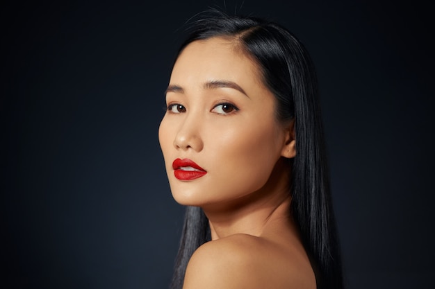 Aziatisch vrouwelijk model met rode make-up tegen zwarte achtergrond.