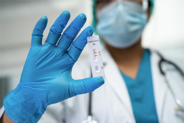 Aziatische arts in pbm-pak toont positief testresultaat met saliva antigen test kit voor controle covid19 coronavirus in ziekenhuis