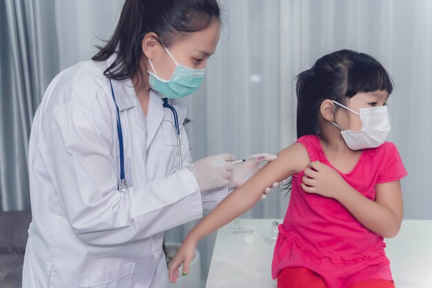 Aziatische arts-injectievaccin voor de bescherming van virus covid19 voor een meisje draagt een medisch maskerMensen zijn meisjes worden elk jaar ingeënt tegen griep