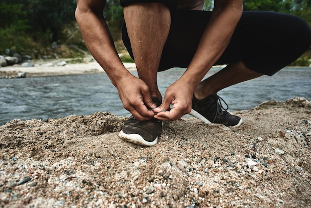 Aziatische atleet die schoenveters bindt voor een ochtendjoggen op de rivier, Kazachse jogger in de natuur close-up