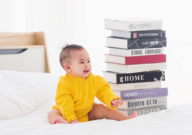 Aziatische baby schattig klein meisje peuter kijkt naar een stapel boeken op slaapkamer wit bed Eerste baby bibliotheek concept