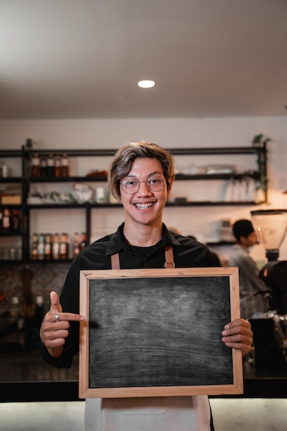 Aziatische barista die een bord vasthoudt en wijst als hij voor de pub staat