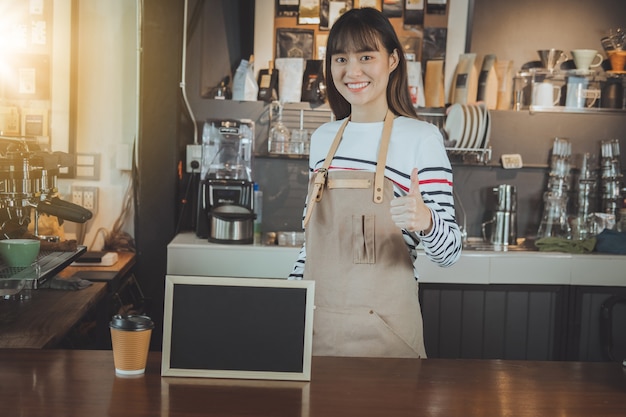 Aziatische barista die zich bij tegenbar en hand bevindt die duim toont