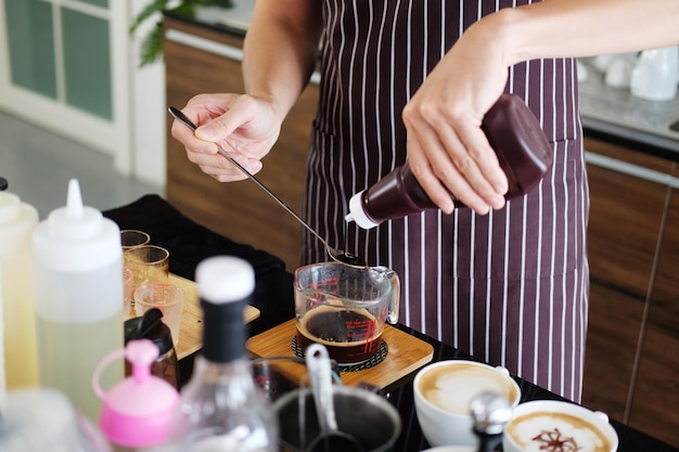 Aziatische barista jongeman lacht en giet verse chocolade in een glazen beker om koffie te maken