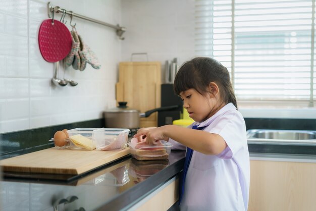 Aziatische basisschool student meisje in uniform sandwich maken voor lunchdoos in de ochtendschool routine voor dag in het leven klaar voor school.