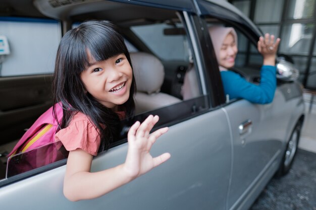 Aziatische basisschoolleerling die in de auto zit en vaarwel zwaait terwijl hij 's ochtends naar school gaat