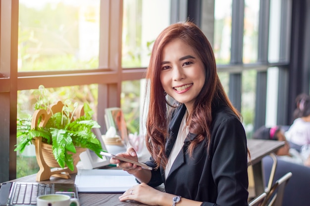 Aziatische bedrijfsvrouwen die notitieboekje en slimme telefoon en het bedrijfsvrouwen glimlachen gelukkig voor het werken gebruiken