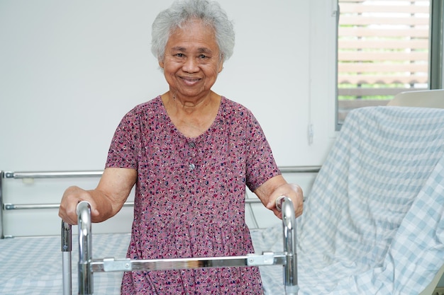 Aziatische bejaarde gehandicaptenpatiënt loopt met rollator in medisch concept voor verpleegziekenhuizen