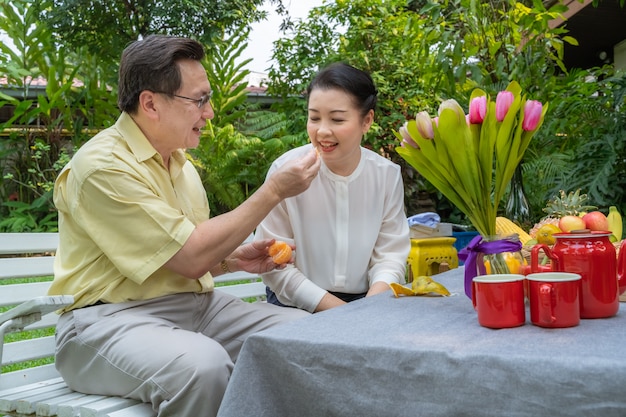 Foto aziatische bejaarde stellen zorgen voor elkaar door sinaasappels te stropen om te eten. familieconcept, parenconcept