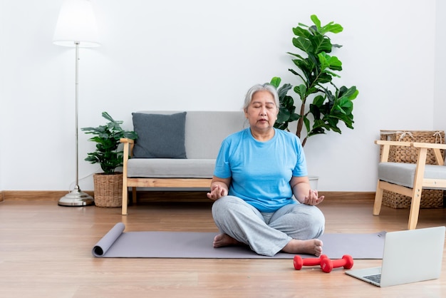 Aziatische bejaarde vrouw beoefent yoga in de basispositie in haar woonkamer