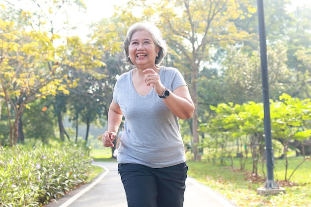 Aziatische bejaarde vrouw die 's ochtends in het park jogt, lacht ze gelukkig gezond lichaam. concept van gezondheidszorg voor senioren om gezond te zijn