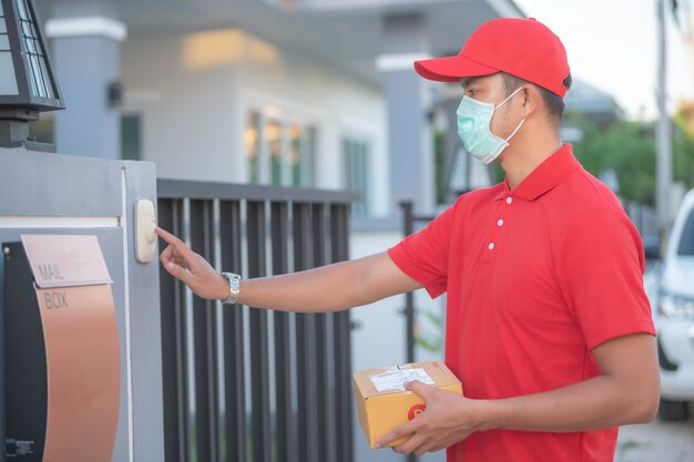 Aziatische bezorger draagt beschermend masker in rood uniform Online voedsel- en productbezorgingsconcept Nieuw normaal in covid19