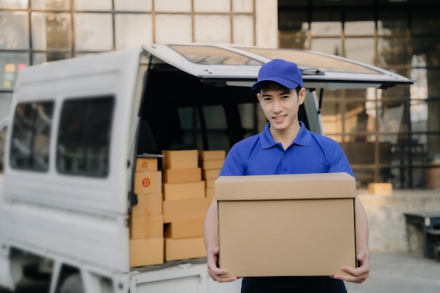 Aziatische bezorger portret van een jonge man die een kartonnen doos vasthoudt tijdens het lossen van een verhuiswagen buiten