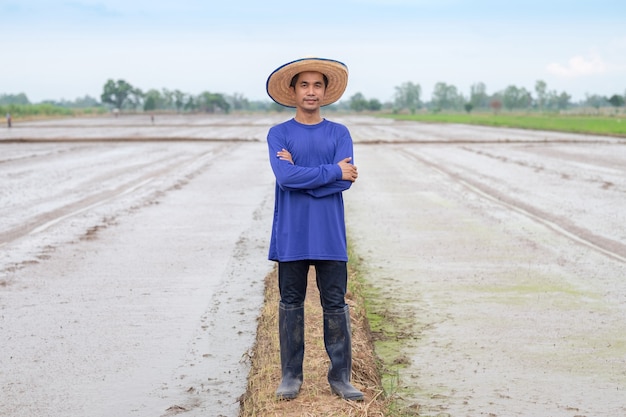 Aziatische boer man draagt een blauw t-shirt en hoed staande rijst kijken naar de boerderij