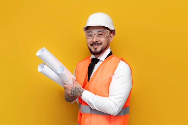 Aziatische bouwer-ingenieur in uniform met papieren met blauwdrukken op gele geïsoleerde achtergrond