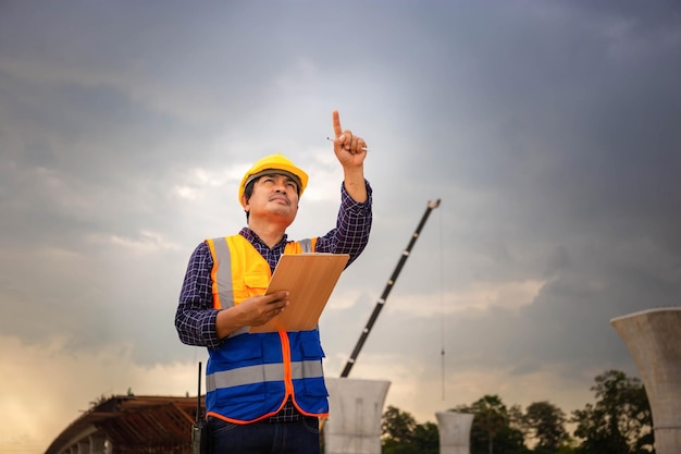 Aziatische bouwingenieur die project controleert op de bouwplaats foreman-arbeider in veiligheidshelm op de bouwplaats van de infrastructuur